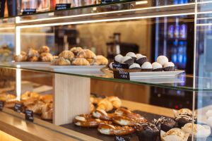 Eine beleuchtete Verkaufstheke mit verschiedenen Backwaren wie Croissants, Muffins, Brezeln und weißen Mandel-Kokos-Bällchen hinter Glas.