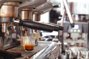 Nahaufnahme einer Espressomaschine, die Kaffee in ein kleines Glas fließen lässt.