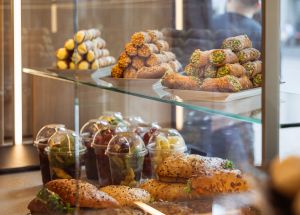 Vitrine mit pyramidenförmig aufgeschichteten Cannoli in verschiedenen Geschmacksrichtungen sowie herzhaften Sandwiches und Obstbechern darunter.