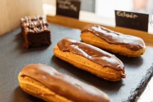 Drei mit Schokoladenguss überzogene Eclairs und ein Schokoladen-Brownie liegen verkaufsbereit auf einer dunklen Schieferplatte.